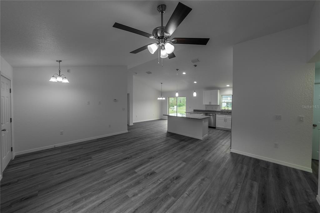 An open-concept living and kitchen area features gray wood-look flooring and a ceiling fan — 11 MALAUKA PASS, OCKLAWAHA, FL