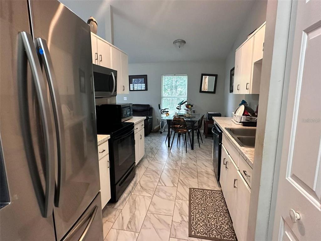 A galley-style kitchen features white cabinets, stainless steel appliances, and light-colored marble-patterned tile flooring — 1021 EMBRUN COURT, KISSIMMEE, FL