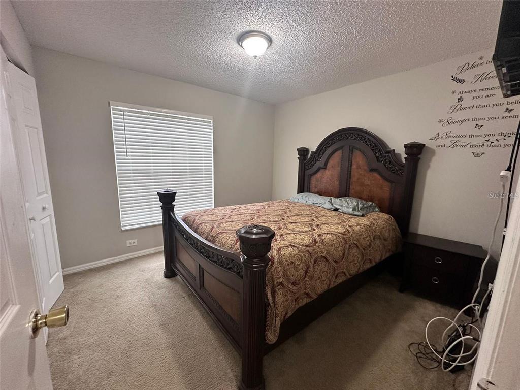 A bedroom features a dark wood bed frame, beige carpet, and a wall decal — 1021 EMBRUN COURT, KISSIMMEE, FL