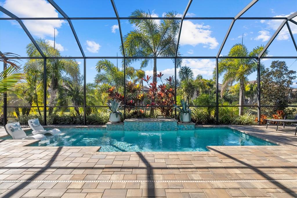 A swimming pool with a water feature and lounge chairs inside a screened-in patio — 10003 BATCHELDER TERRACE, PALMETTO, FL