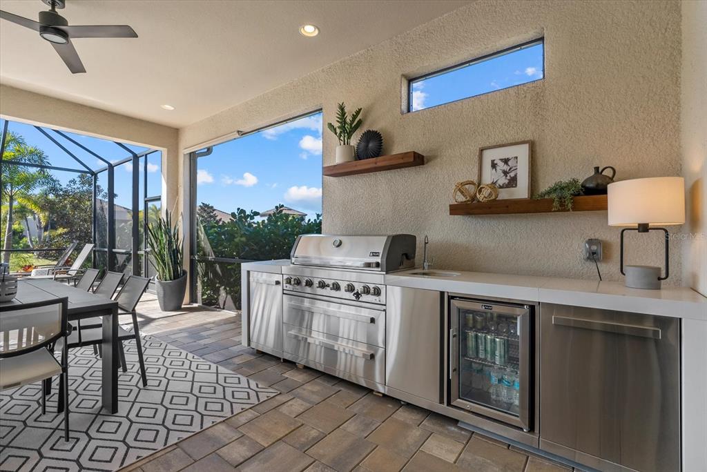 An outdoor kitchen features stainless steel appliances, a sink, and shelving against a textured wall — 10003 BATCHELDER TERRACE, PALMETTO, FL