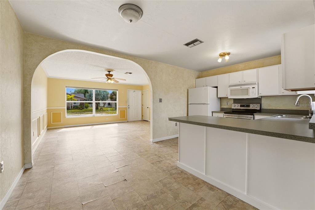 A kitchen with white cabinets and a breakfast bar opens into a living room area — 6399 CONISTON STREET, PORT CHARLOTTE, FL