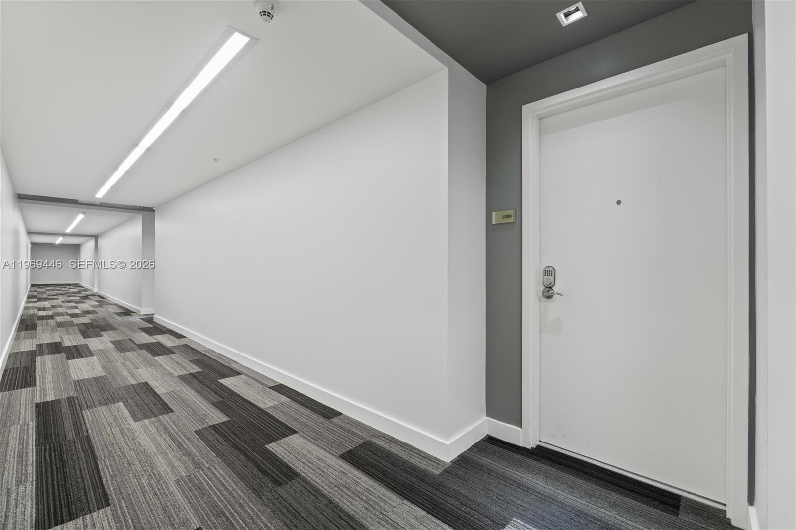 A long hallway features white walls, a patterned gray carpet, and a white door — 3301 NE 1st Ave # L0304, Miami FL 33137, MIAMI, FL