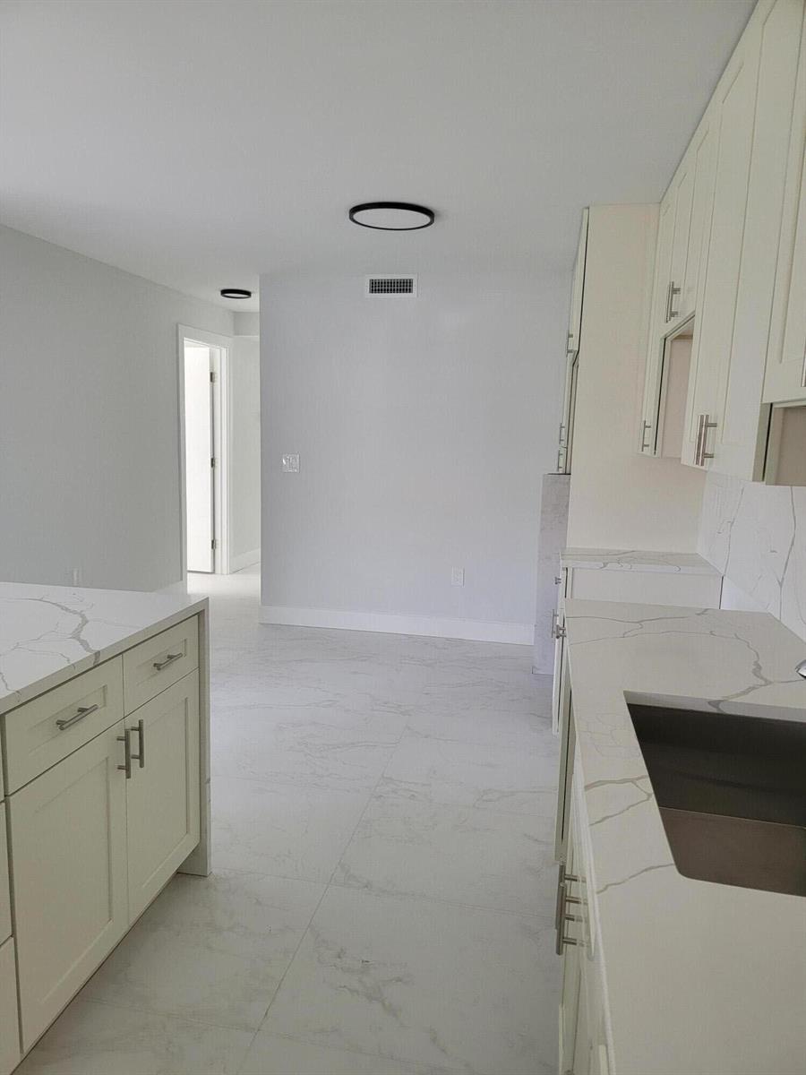 A modern kitchen features white cabinets, marble-patterned countertops, and light-colored tile flooring — 240 SW 7th Street # 9, Boca Raton FL 33432, BOCA RATON, FL
