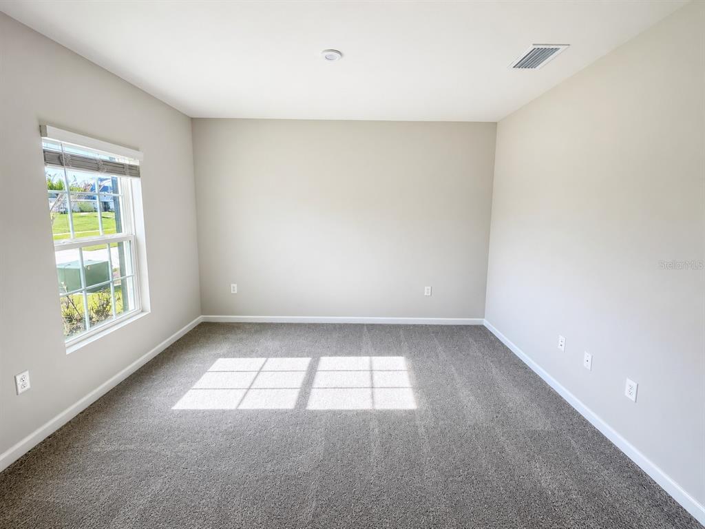 An empty bedroom with beige walls, gray carpet, and a window overlooking a neighborhood — 4213 CATTAIL MARSH DRIVE, LAKELAND, FL