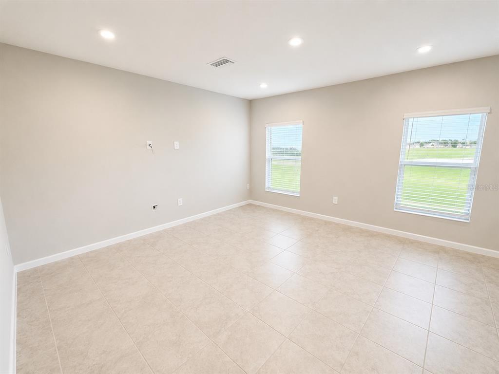 An empty room with beige walls, light-colored tile flooring, recessed lighting, and two windows — 4213 CATTAIL MARSH DRIVE, LAKELAND, FL