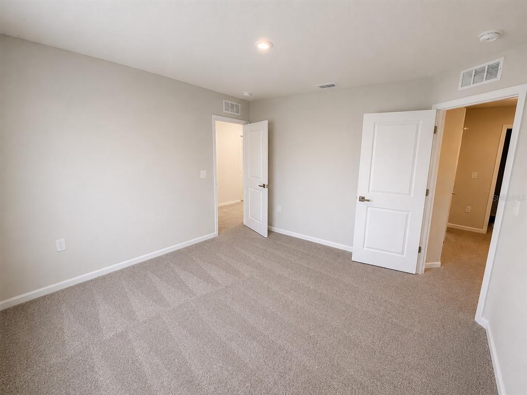 An empty bedroom features beige walls, gray carpeting, two open white doors, and recessed lighting — 4213 CATTAIL MARSH DRIVE, LAKELAND, FL