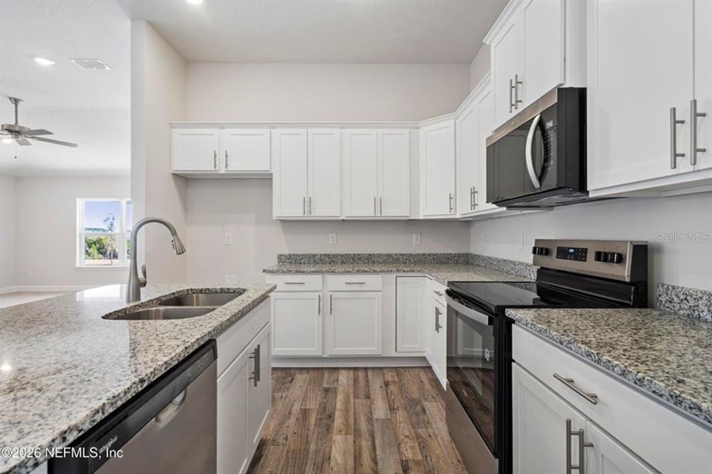 A kitchen features white cabinets, granite countertops, stainless steel appliances, and wood-look flooring — 16 BEAVERDAM LANE, PALM COAST, FL