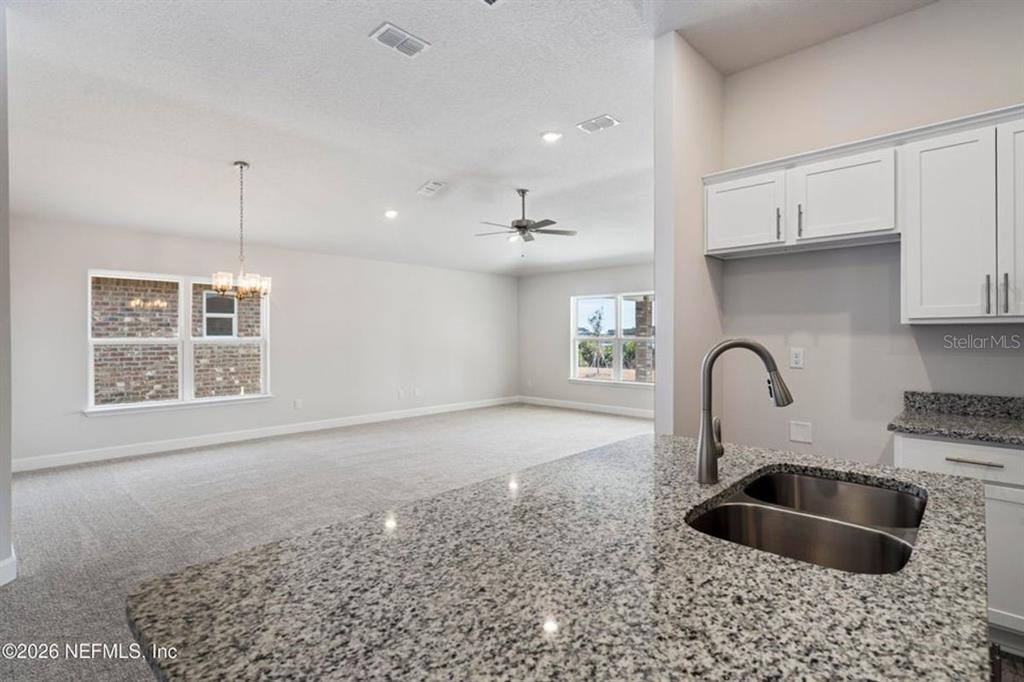 A kitchen island with a granite countertop overlooks an open-concept living and dining area — 16 BEAVERDAM LANE, PALM COAST, FL