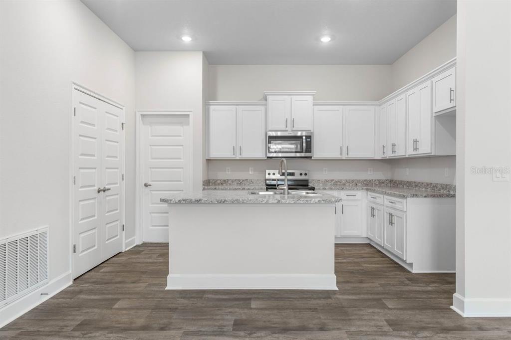 A kitchen with white cabinets, granite countertops, a center island, and wood-look flooring — 16 BEAVERDAM LANE, PALM COAST, FL