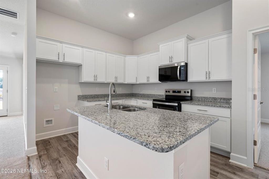 A kitchen features white cabinets, granite countertops, a center island, and stainless steel appliances — 16 BEAVERDAM LANE, PALM COAST, FL