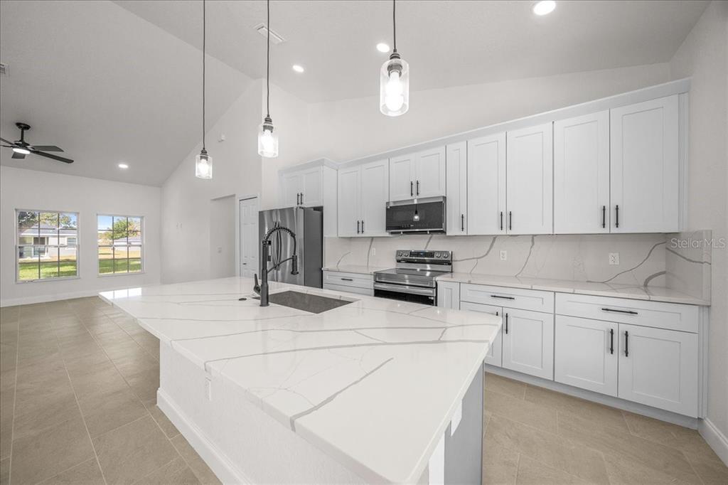 A modern kitchen features white cabinetry, a large marble-topped island, and stainless steel appliances — 13074 SW 104, DUNNELLON, FL