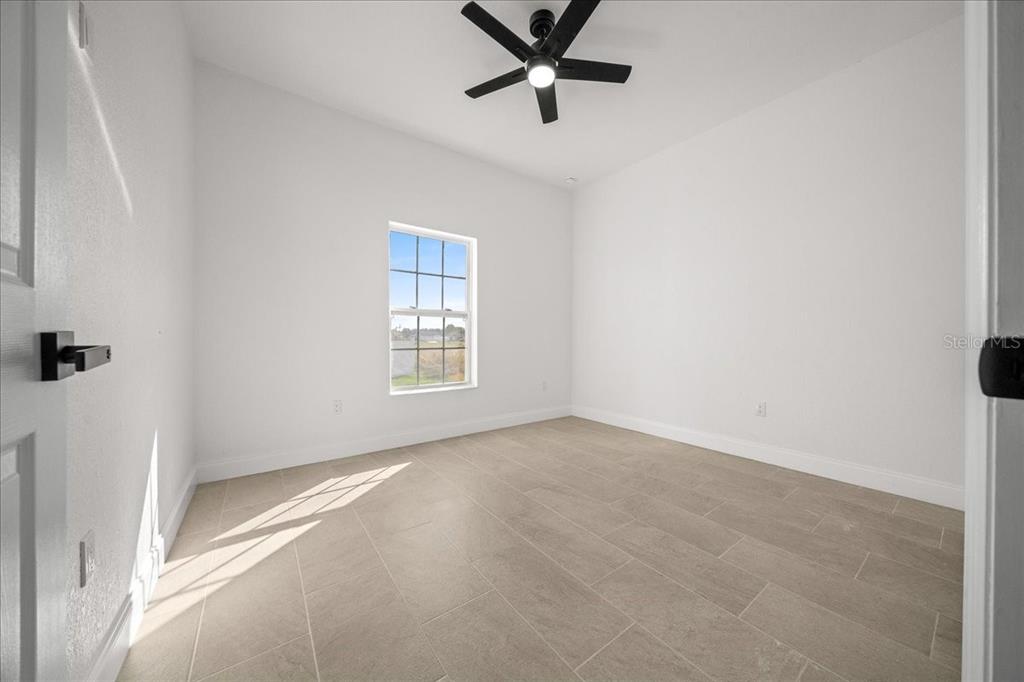 An empty room features white walls, a ceiling fan, and light-colored tile flooring — 13074 SW 104, DUNNELLON, FL