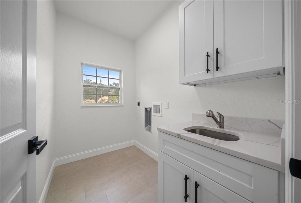 A laundry room features white cabinets, a sink, a window, and light-colored tile flooring — 13074 SW 104, DUNNELLON, FL
