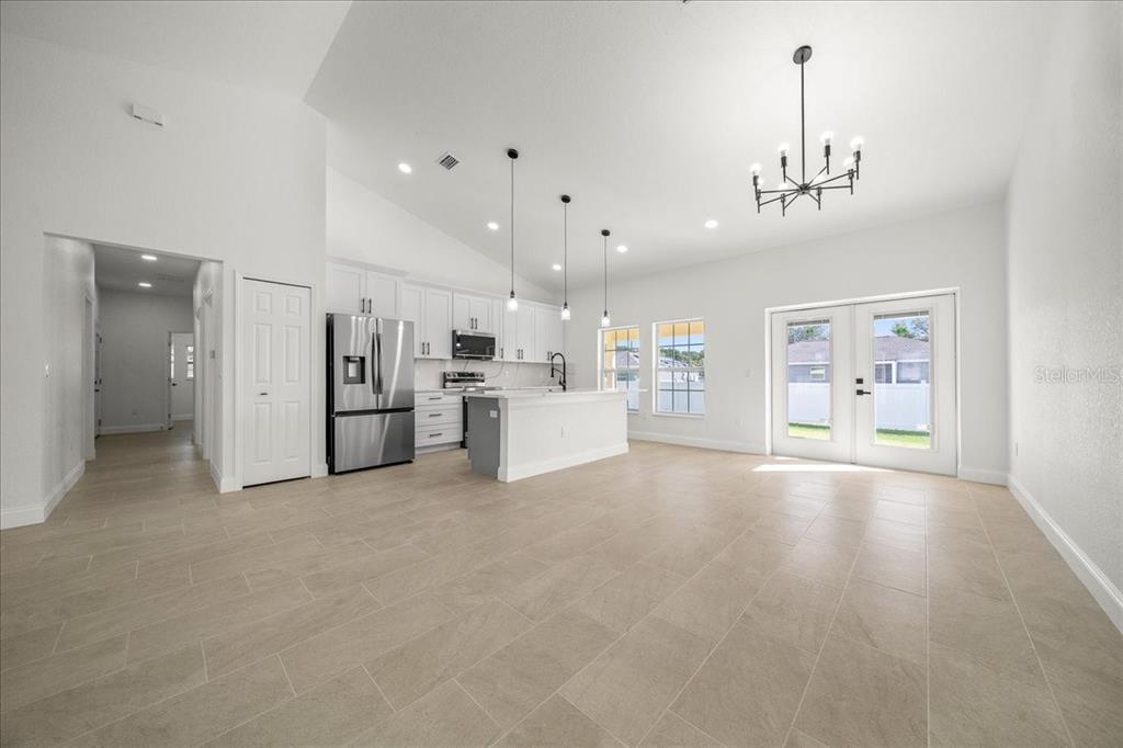 A bright, open-concept kitchen and living area features white cabinetry, stainless appliances, and tile flooring — 13074 SW 104, DUNNELLON, FL