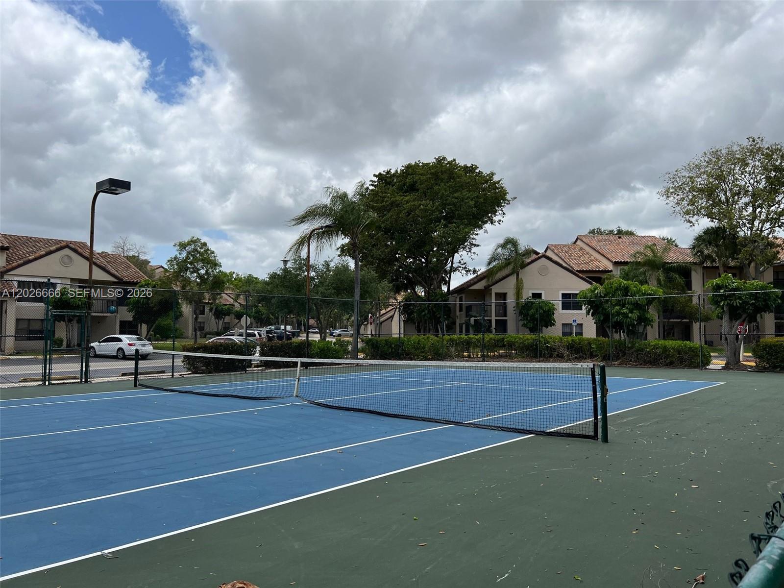 A blue tennis court is surrounded by a chain-link fence and residential apartment buildings — 4581 W Mcnab Rd # 20, Pompano Beach FL 33069, POMPANO BEACH, FL