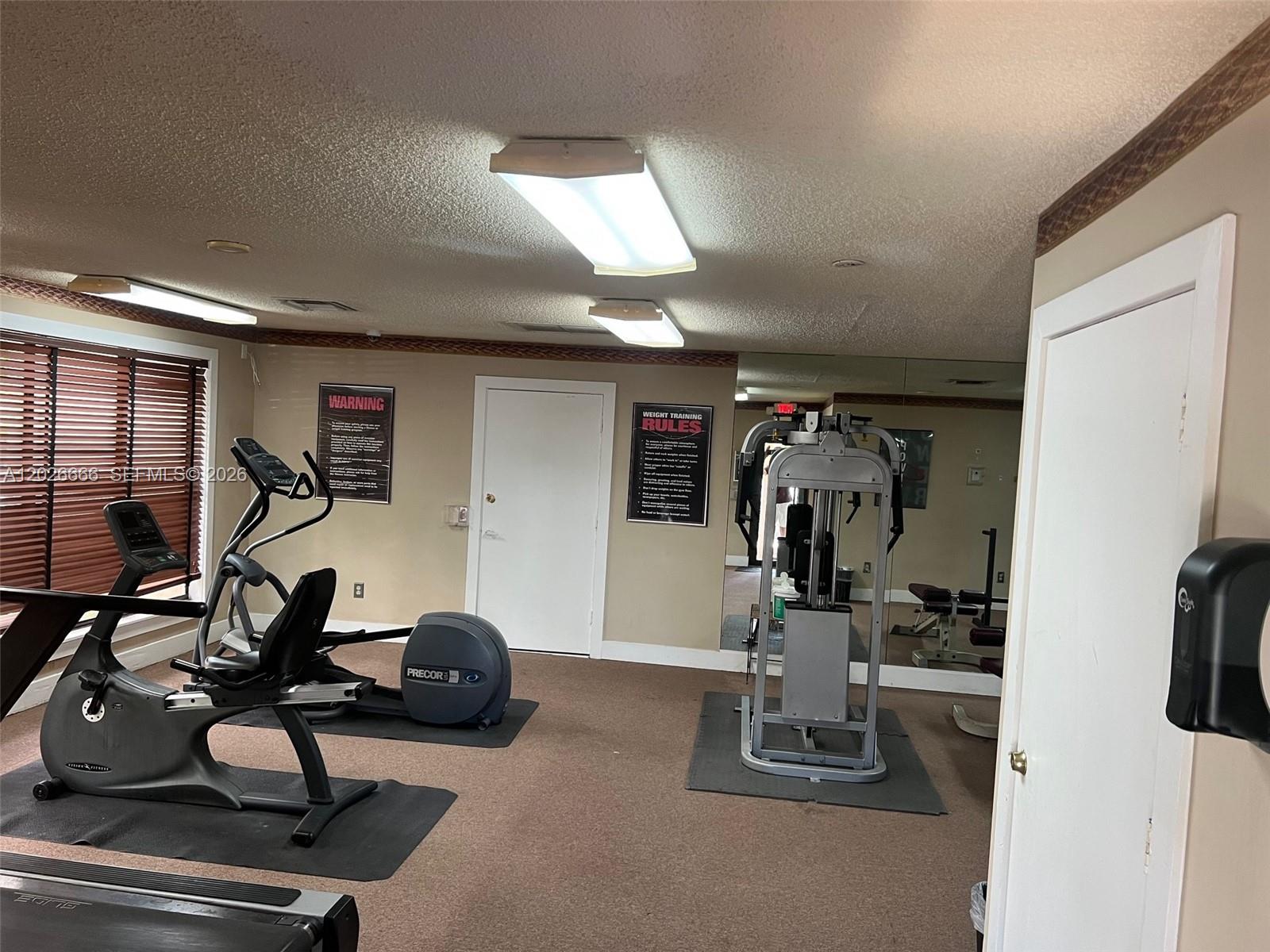 A small gym room features exercise equipment, carpeted flooring, and a mirrored wall — 4581 W Mcnab Rd # 20, Pompano Beach FL 33069, POMPANO BEACH, FL