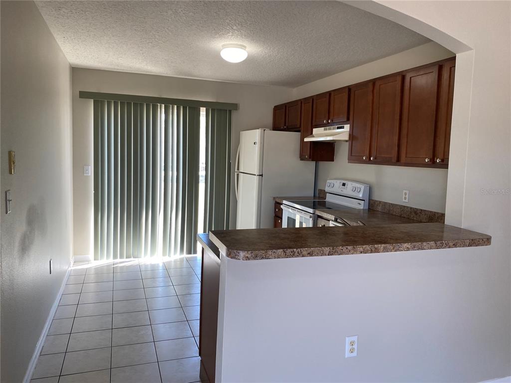 A kitchen with wood cabinets, laminate countertops, and tile flooring next to a sliding door — 1830 2ND STREET NW UNIT B, WINTER HAVEN, FL