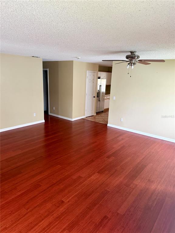 A spacious living area features reddish-brown wood flooring, beige walls, and a ceiling fan — 1326 AGUACATE COURT, ORLANDO, FL