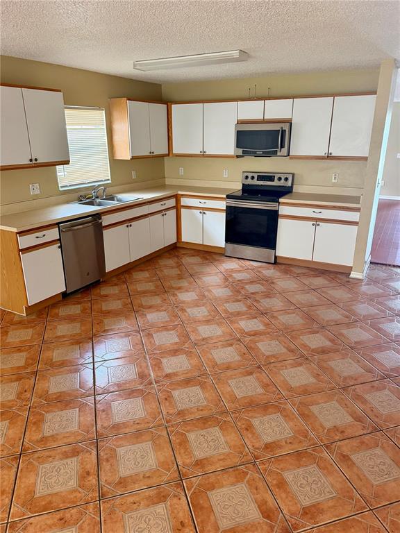 A kitchen features white cabinets, stainless steel appliances, and patterned terracotta-colored floor tiles — 1326 AGUACATE COURT, ORLANDO, FL