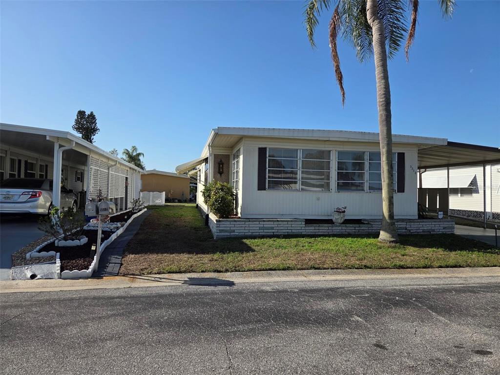 A single-story manufactured home with a white exterior, a palm tree, and a carport — 3312 OVERCUP OAK TERRACE, SARASOTA, FL