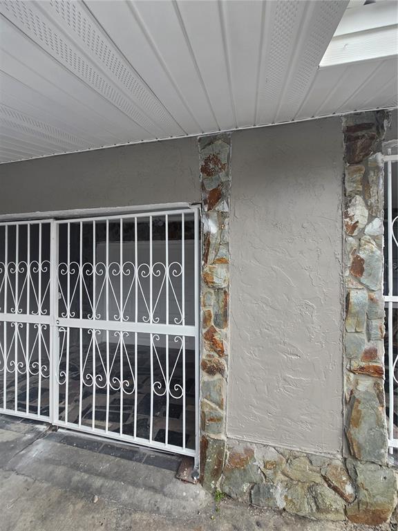 A covered patio area features a white metal security gate and stone-accented stucco walls — 3905 E OSBORNE AVENUE, TAMPA, FL