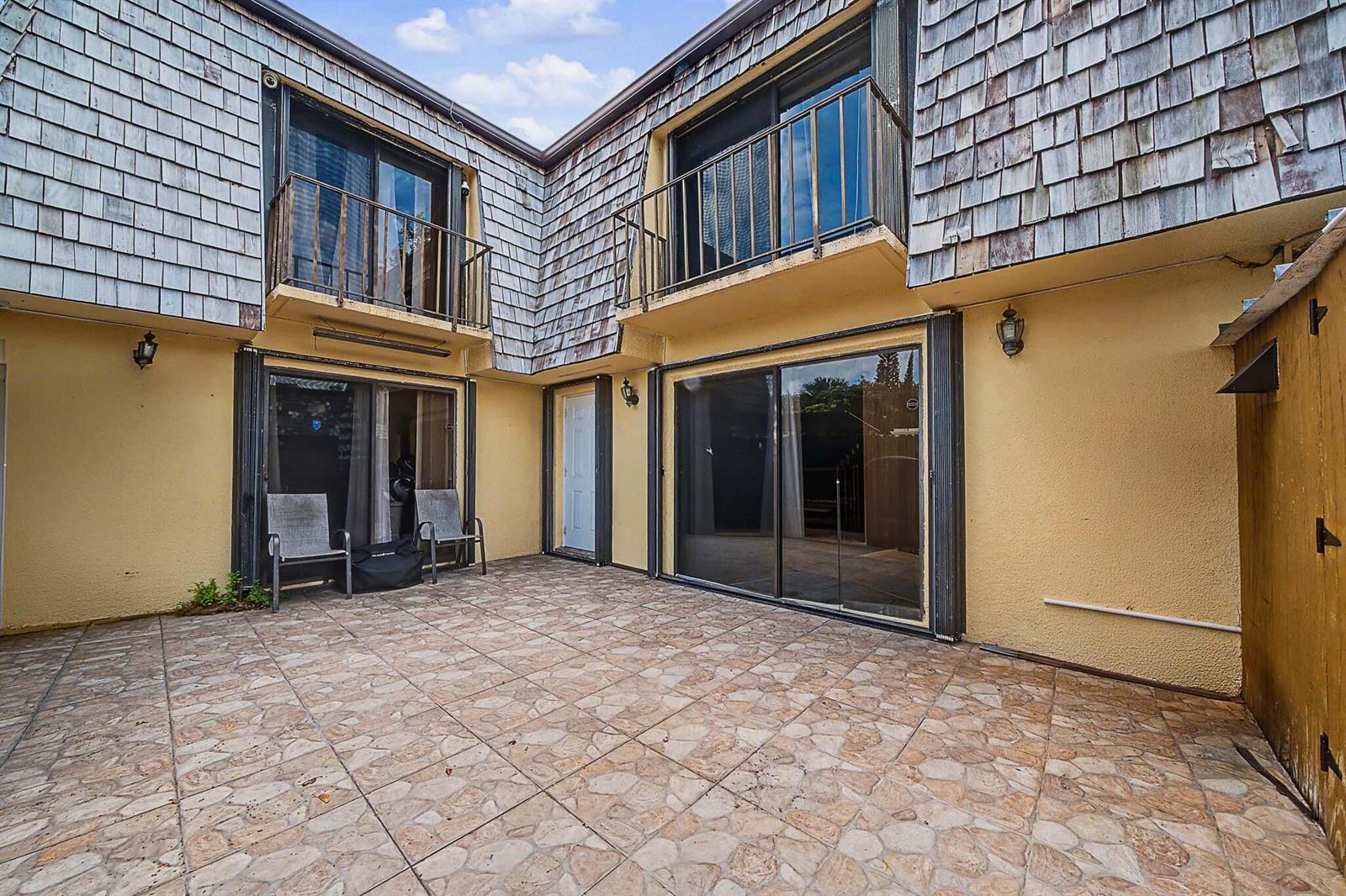A paved patio area sits between two levels of a building with wood-shingled siding — 149 Lake Arbor Drive, Palm Springs FL 33461, PALM SPRINGS, FL