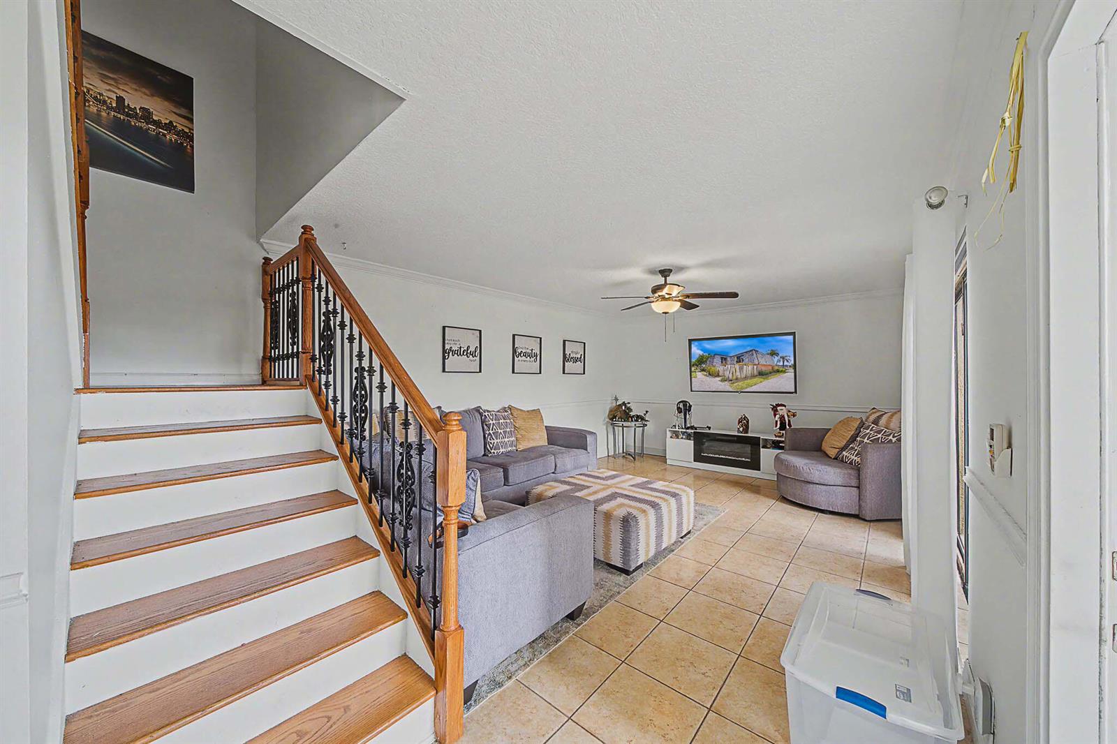 A living room features a staircase with a wood railing, tile flooring, and gray furniture — 149 Lake Arbor Drive, Palm Springs FL 33461, PALM SPRINGS, FL