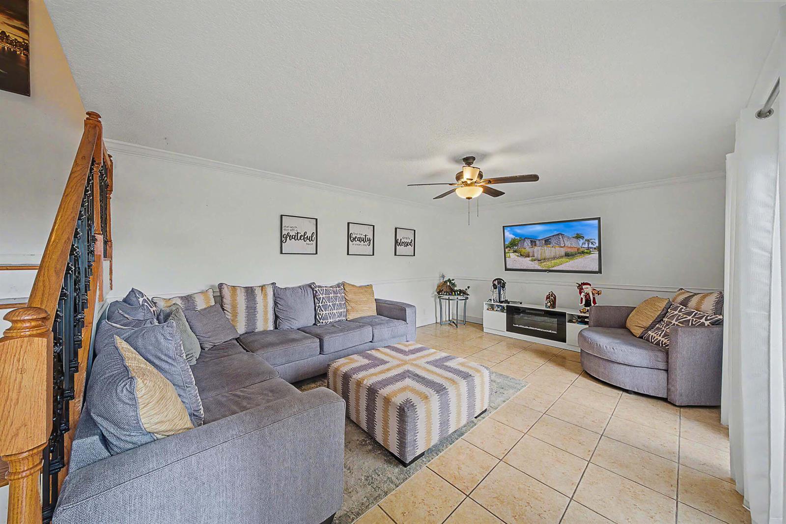 A living room features a gray sectional sofa, a patterned ottoman, and a wall-mounted television — 149 Lake Arbor Drive, Palm Springs FL 33461, PALM SPRINGS, FL