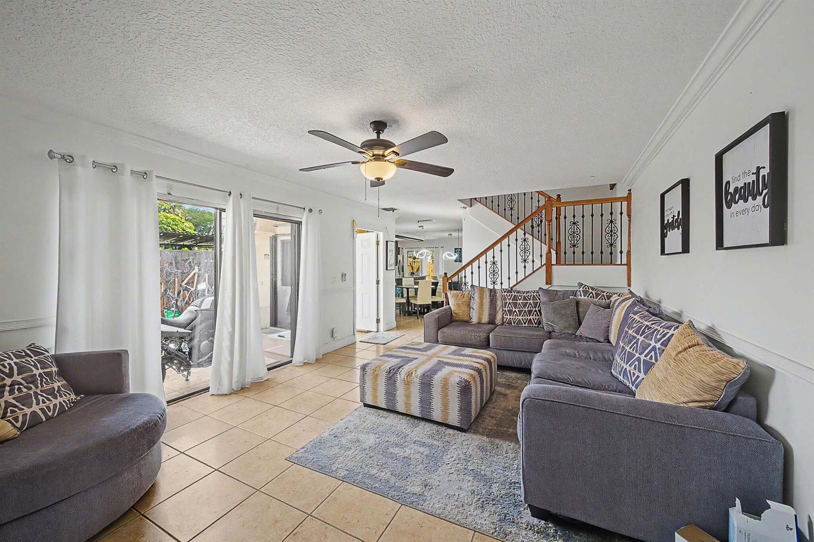 A living room with tile floors, a gray sectional sofa, and a staircase with railing — 149 Lake Arbor Drive, Palm Springs FL 33461, PALM SPRINGS, FL