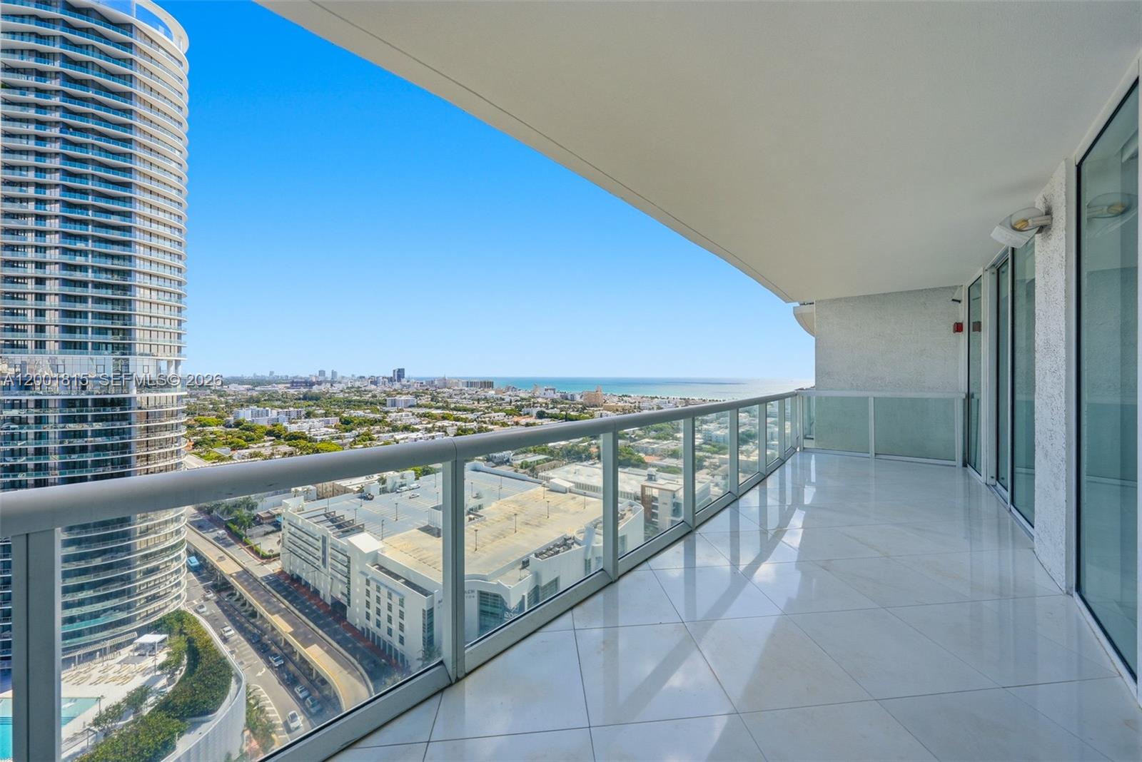 A high-rise balcony with white tile flooring, glass railings, and a panoramic city and ocean view — 450 Alton Rd # 2704, Miami Beach FL 33139, MIAMI BEACH, FL