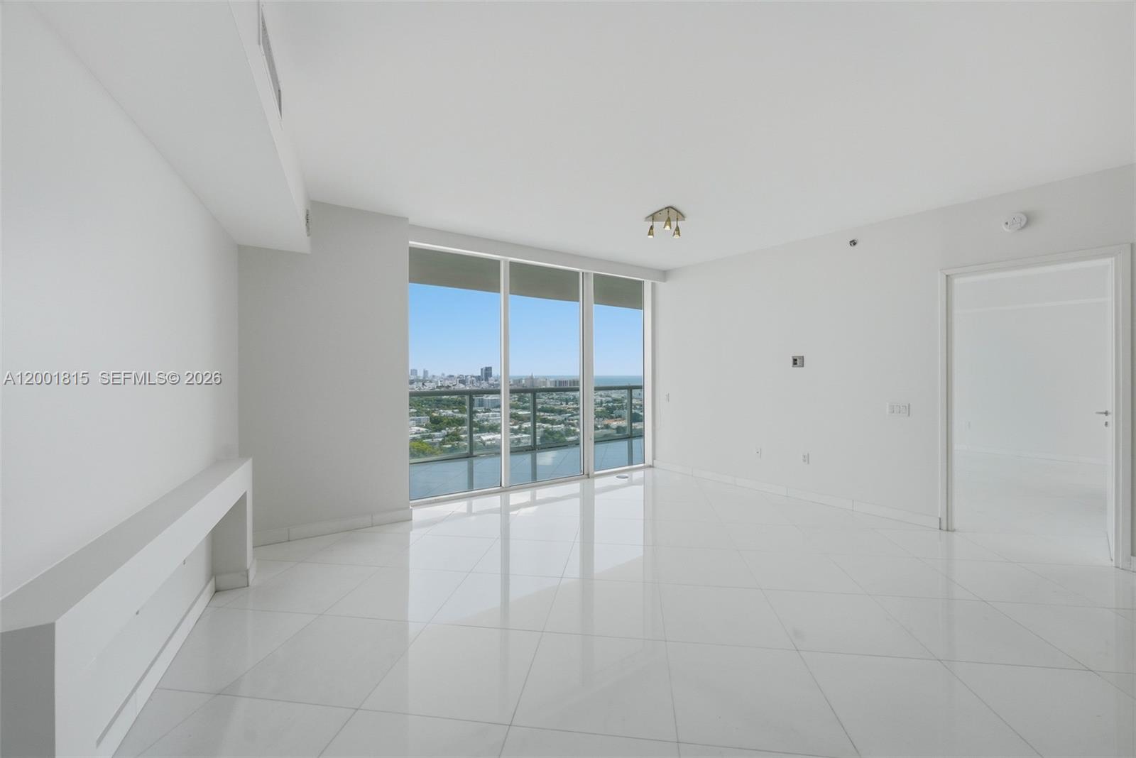 An empty room features white tile floors, white walls, and floor-to-ceiling windows with city views — 450 Alton Rd # 2704, Miami Beach FL 33139, MIAMI BEACH, FL