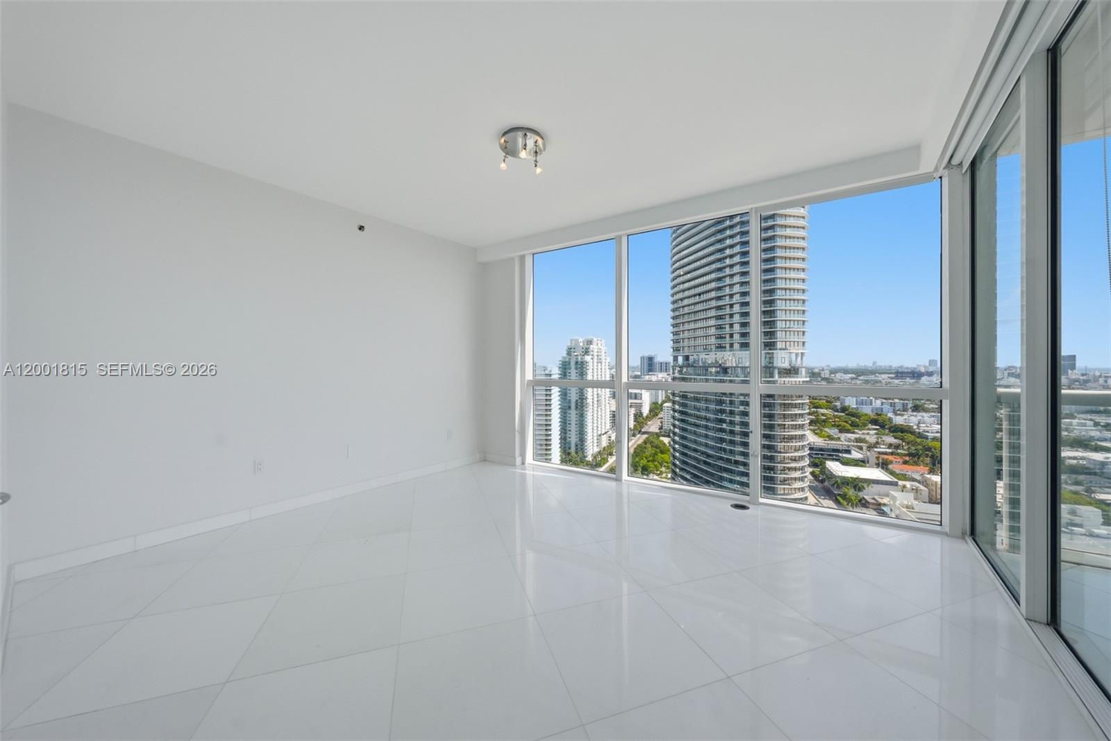 An empty room features white tile floors, white walls, and floor-to-ceiling windows with city views — 450 Alton Rd # 2704, Miami Beach FL 33139, MIAMI BEACH, FL