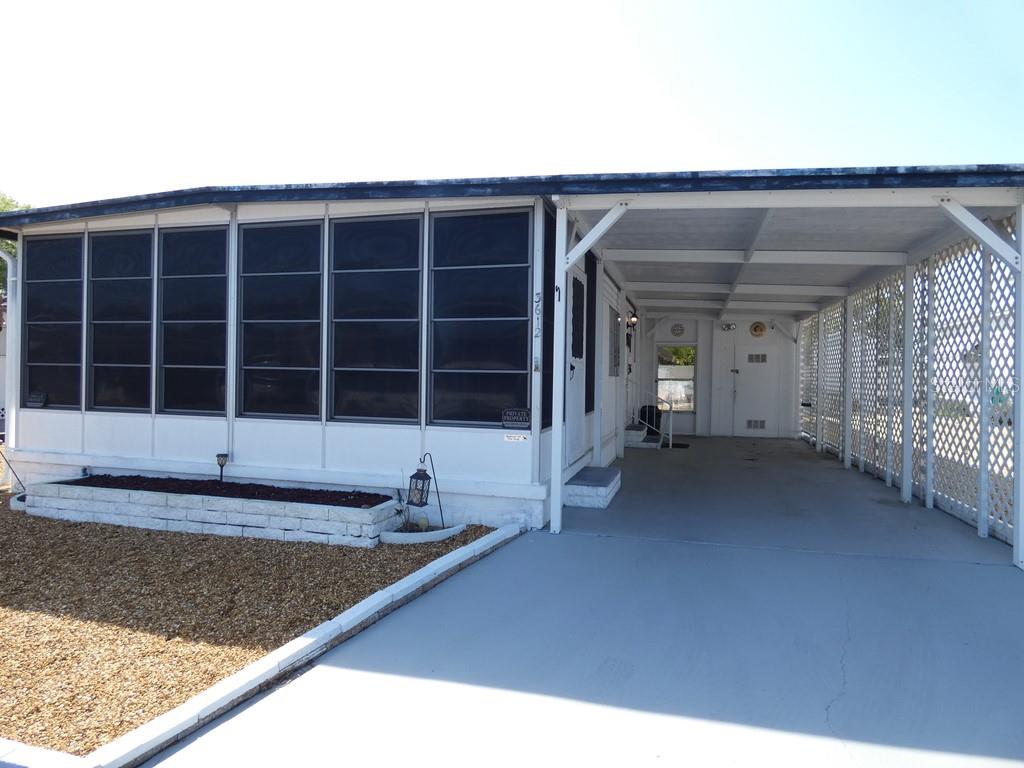 A mobile home exterior features a screened-in porch, a concrete driveway, and a covered carport — 3612 TIKI DRIVE, HOLIDAY, FL