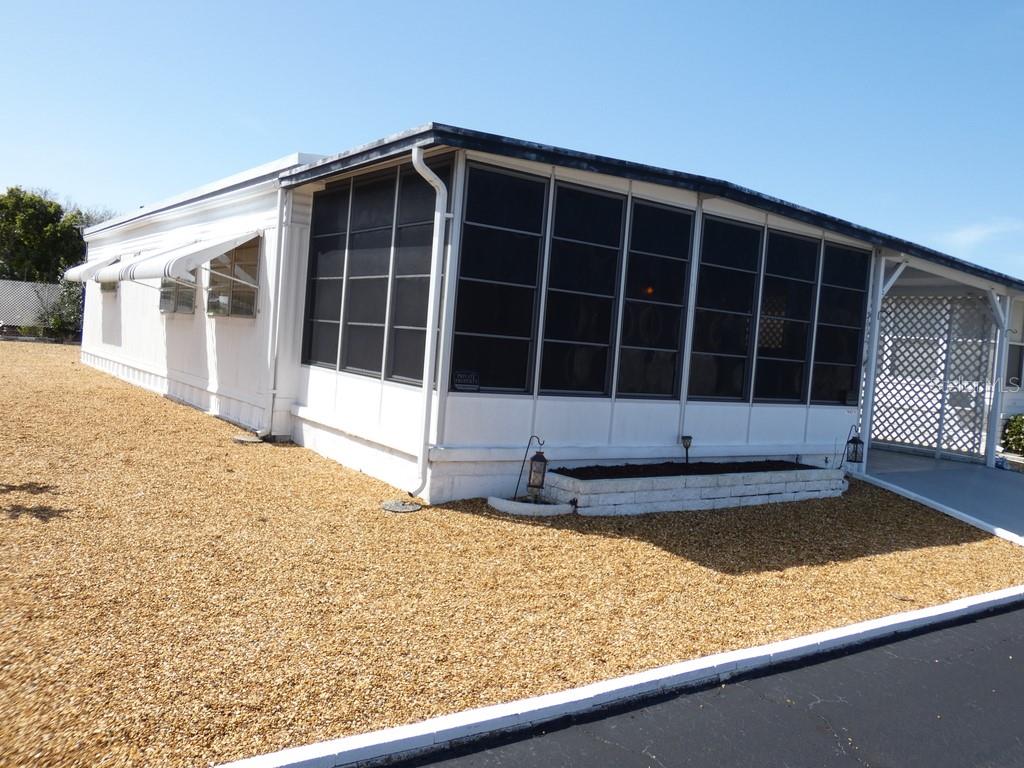 A white mobile home features a screened-in porch, a gravel yard, and a covered carport — 3612 TIKI DRIVE, HOLIDAY, FL