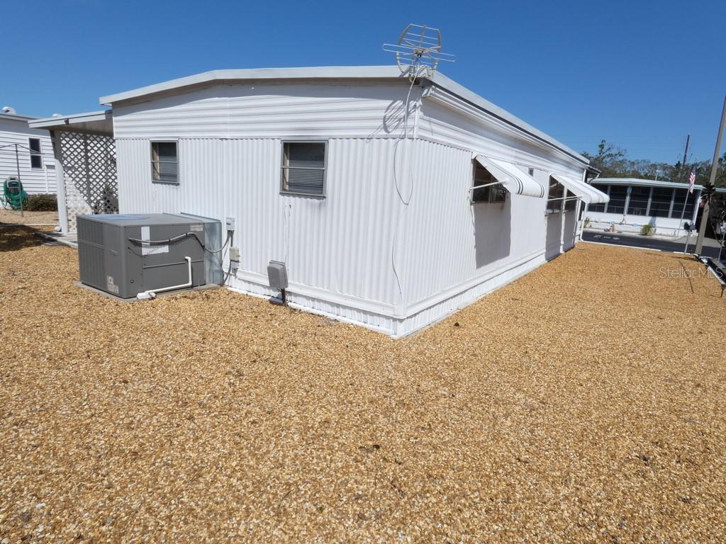 The exterior of a white mobile home features a gravel yard and an HVAC unit — 3612 TIKI DRIVE, HOLIDAY, FL