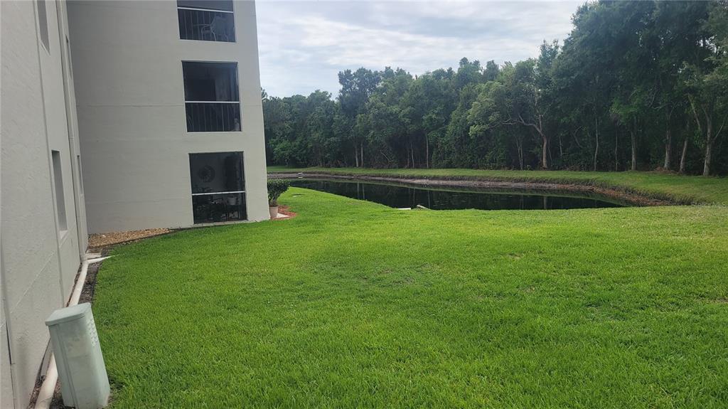 A multi-story apartment building exterior overlooks a grassy lawn and a small pond — 2737 E ENTERPRISE ROAD UNIT 151, CLEARWATER, FL