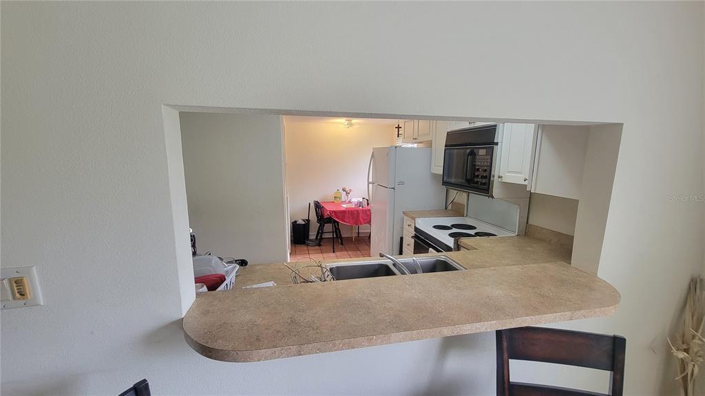 A kitchen pass-through window overlooks a dining area with a table and white refrigerator — 2737 E ENTERPRISE ROAD UNIT 151, CLEARWATER, FL