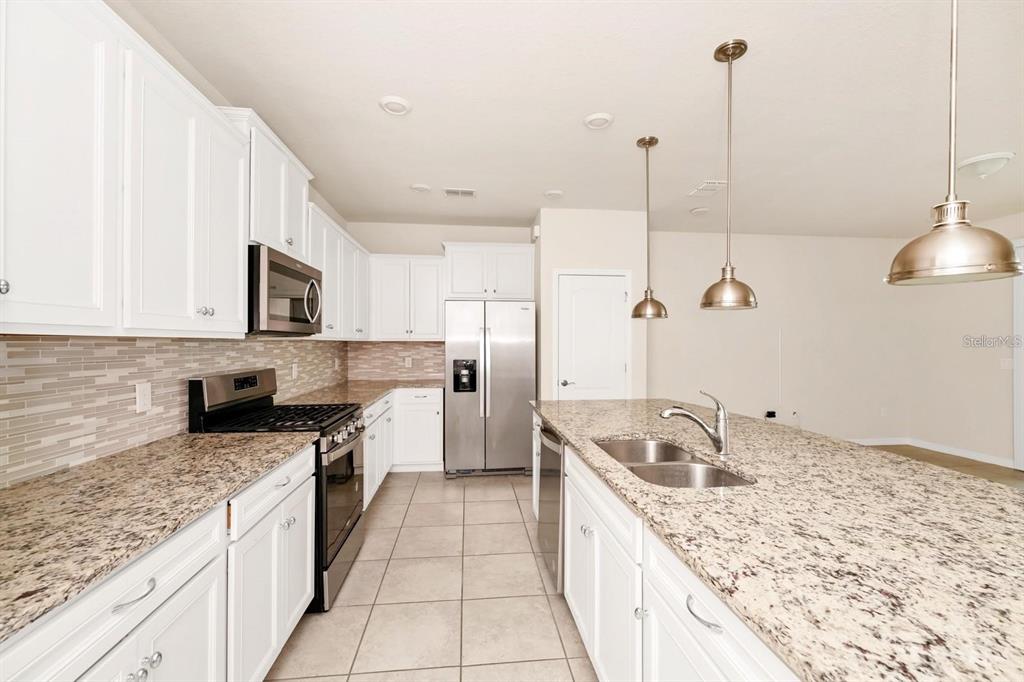 A kitchen features white cabinets, granite countertops, stainless steel appliances, and a central island — 7513 OAK SPRING LANE, DAVENPORT, FL