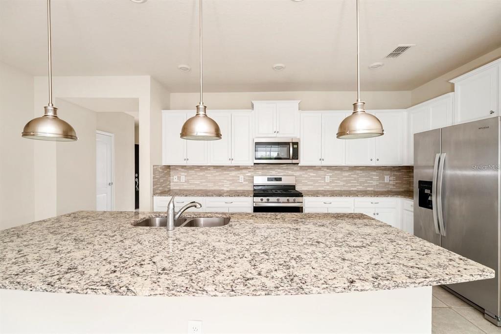 A kitchen features white cabinets, granite countertops, stainless steel appliances, and two hanging pendant lights — 7513 OAK SPRING LANE, DAVENPORT, FL