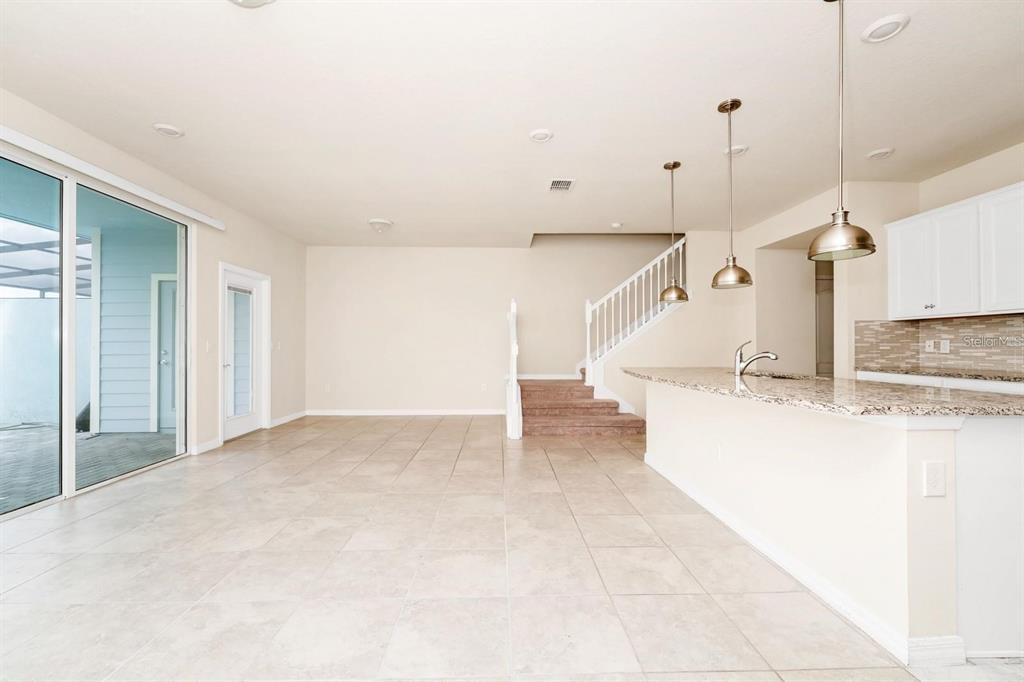 An open-concept kitchen and living area features tile flooring, a granite island, and stairs — 7513 OAK SPRING LANE, DAVENPORT, FL