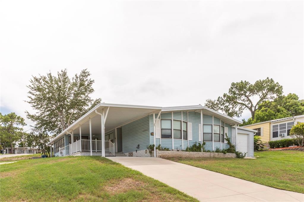 A light blue single-story manufactured home features a covered carport and a concrete driveway — 7379 DEL RIO AVENUE, BROOKSVILLE, FL