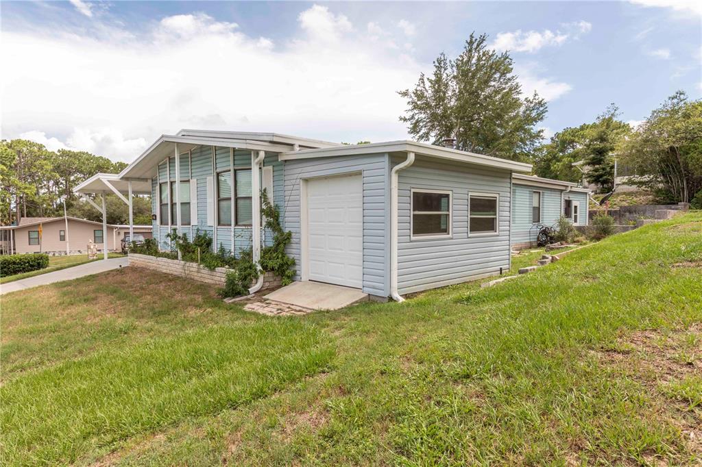 A light blue manufactured home with a white garage door and a covered carport — 7379 DEL RIO AVENUE, BROOKSVILLE, FL