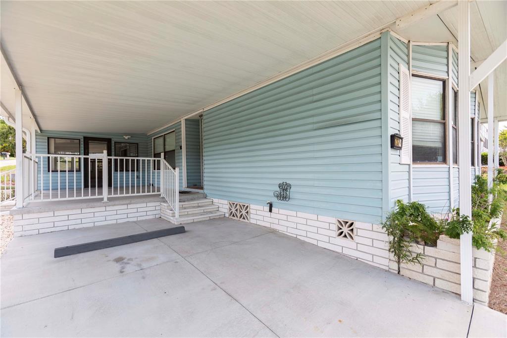 A light blue mobile home features a covered concrete carport and a white brick foundation — 7379 DEL RIO AVENUE, BROOKSVILLE, FL