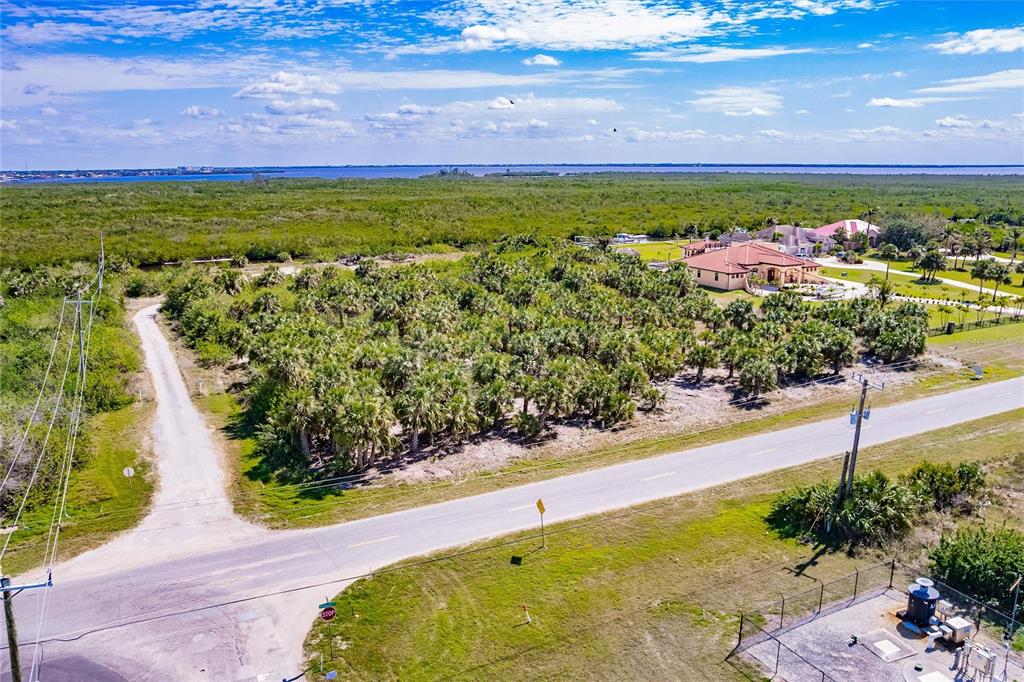An aerial view shows a vacant, palm-covered lot next to a road and a large house — 19155 MIDWAY BOULEVARD, PORT CHARLOTTE, FL