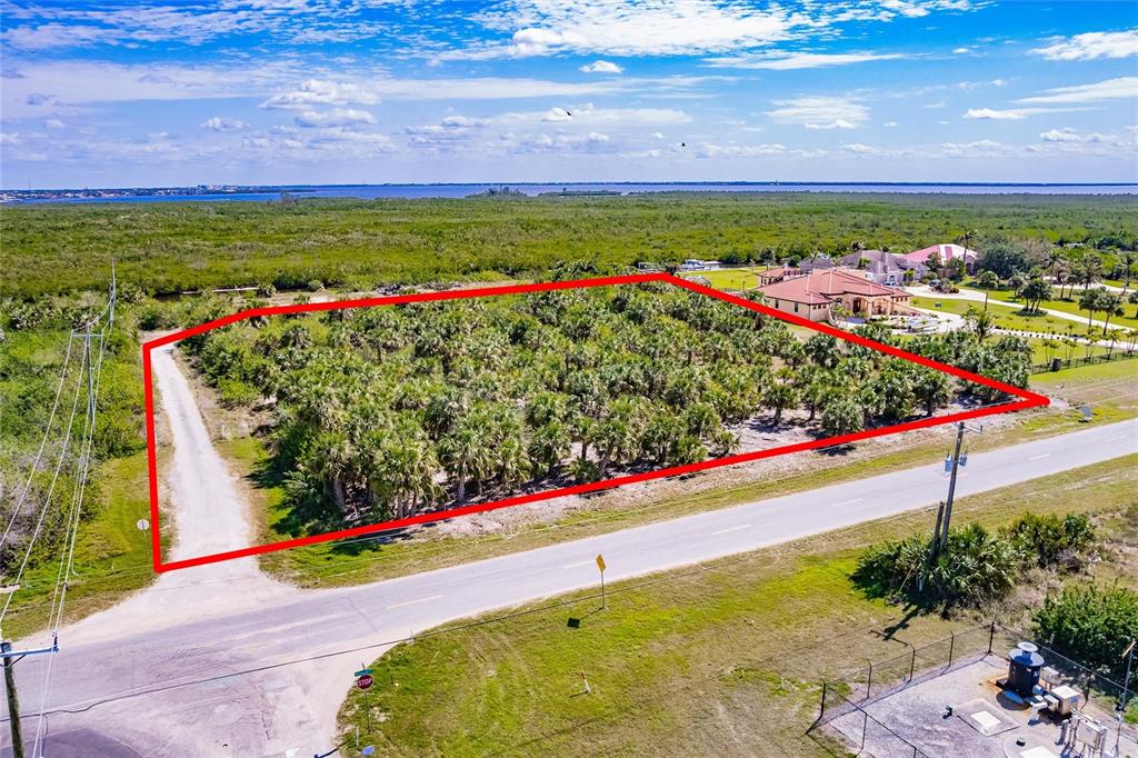 An aerial view shows a rectangular, palm-covered vacant lot outlined in red next to a road — 19155 MIDWAY BOULEVARD, PORT CHARLOTTE, FL