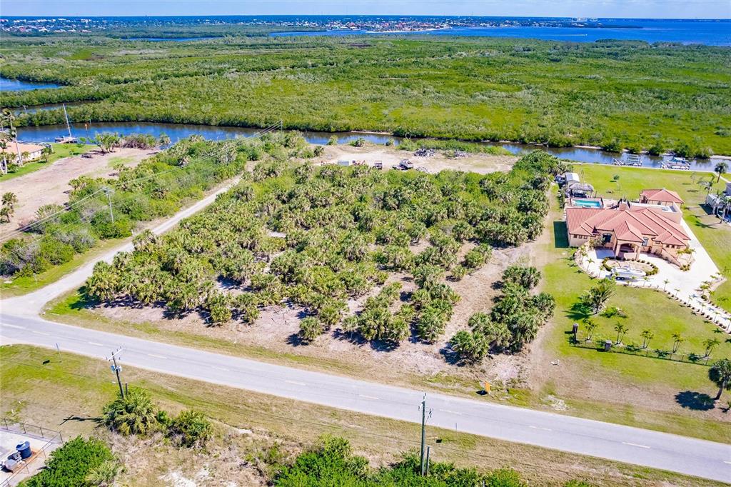 An aerial view shows a vacant, palm-covered lot situated next to a large residential home — 19155 MIDWAY BOULEVARD, PORT CHARLOTTE, FL