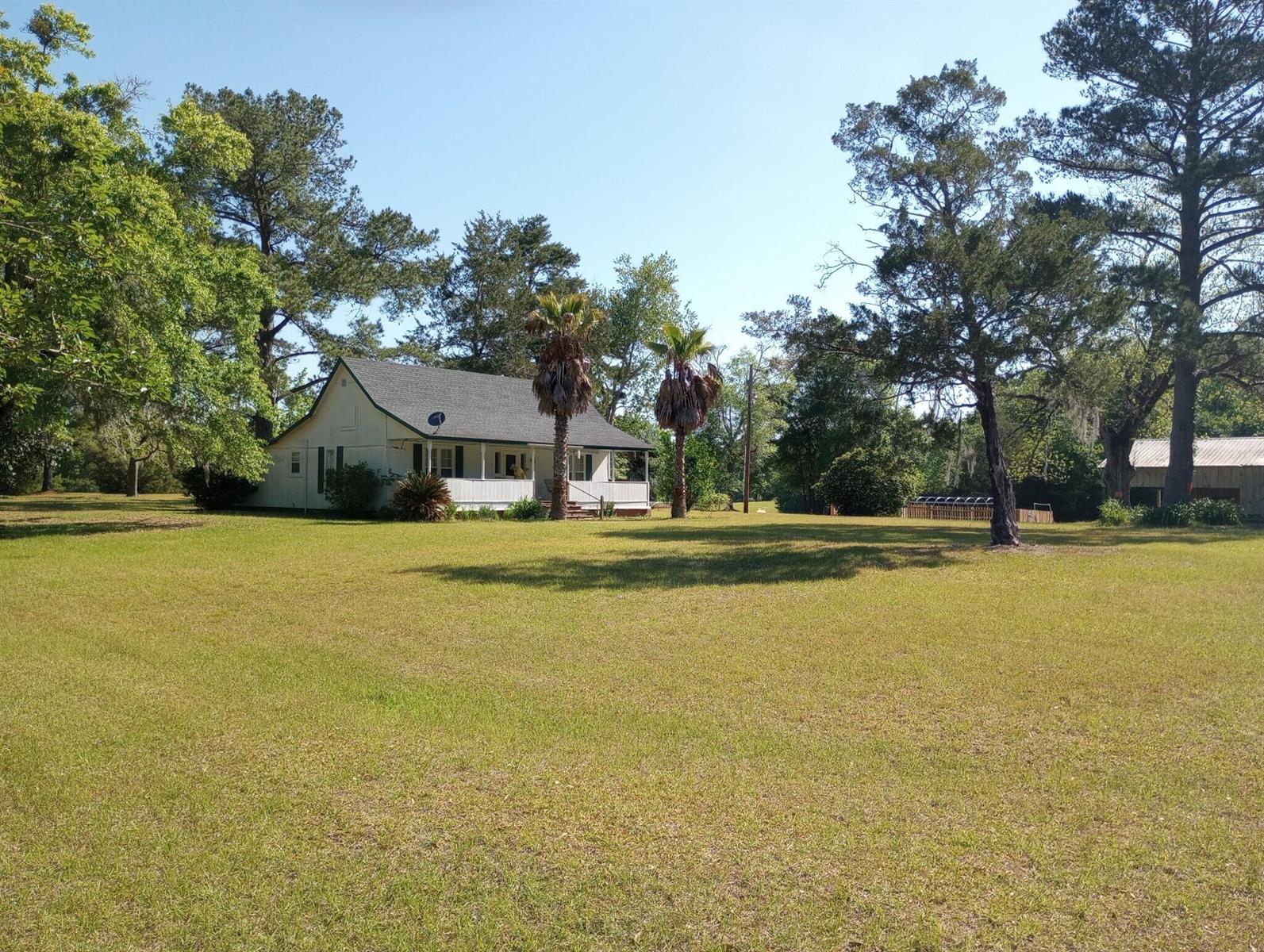 A large grassy lawn leads toward a metal-roofed open-sided shed near a wooded area — 1900 Olive Lane, FL 32425, FL