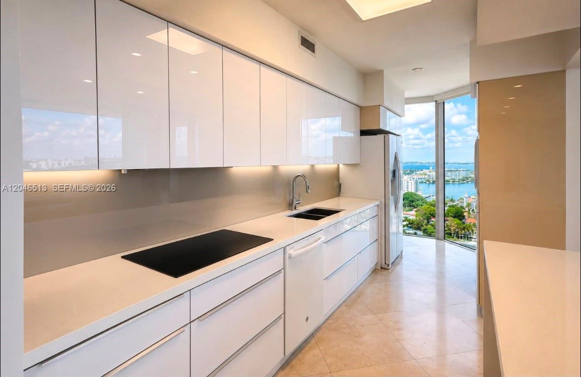 A modern kitchen features white glossy cabinets, light countertops, and a view of the water — 4775 Collins Ave # 2407, Miami Beach FL 33140, MIAMI BEACH, FL