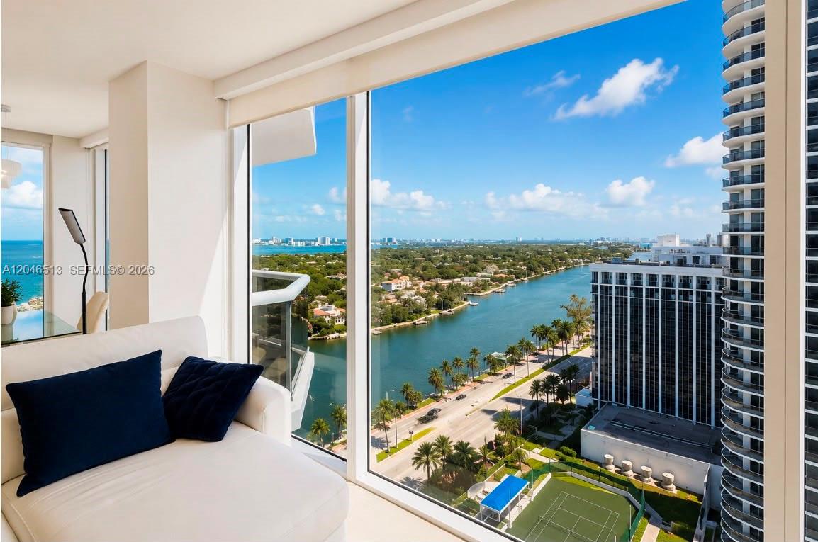 A modern room with a white sofa overlooks a waterway, tennis court, and city skyline — 4775 Collins Ave # 2407, Miami Beach FL 33140, MIAMI BEACH, FL
